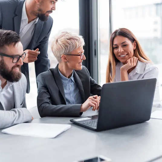 Un grupo de personas están sentadas alrededor de una mesa mirando una computadora portátil.
