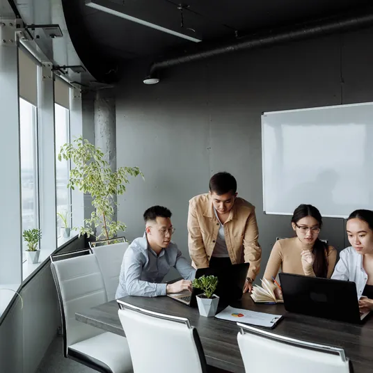 Un grupo de personas está sentada alrededor de una mesa con computadoras portátiles.